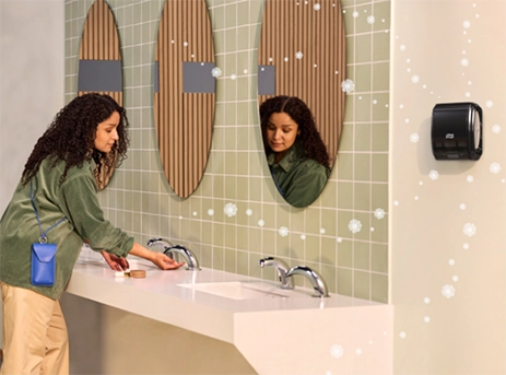 Woman in restroom washing hands near a Tork air freshener wall mounted